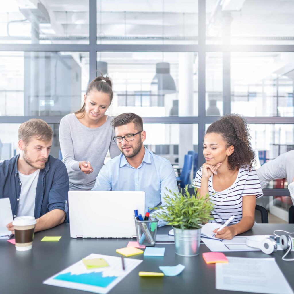 Team members collaborating around a laptop during a workplace meeting.