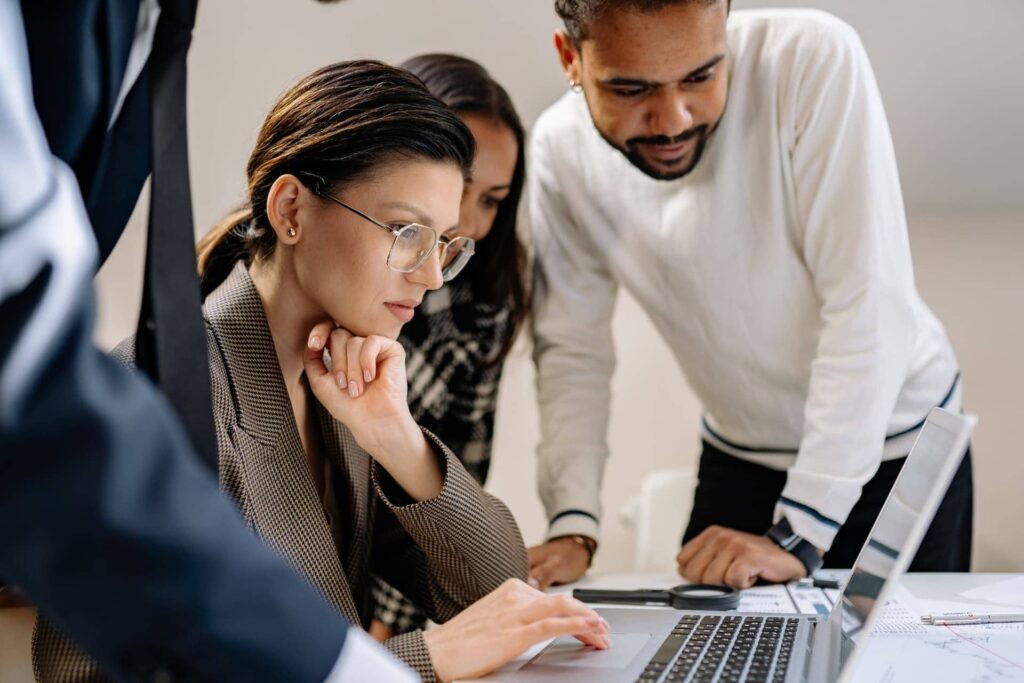 Three colleagues reviewing information together on a laptop during a work discussion.