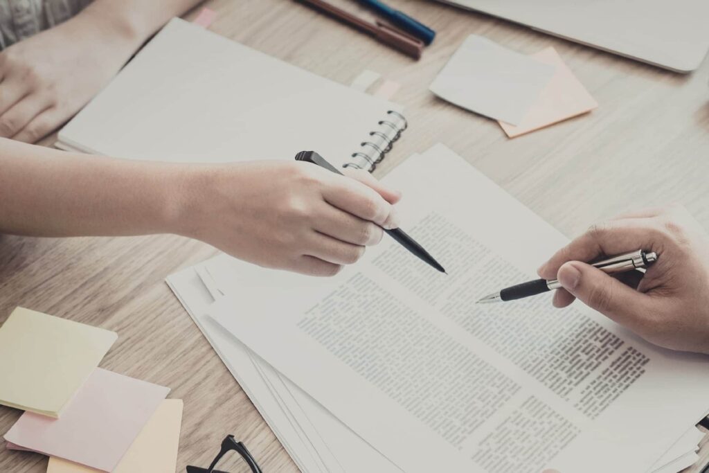 Two people reviewing and discussing documents while pointing at the text with pens.