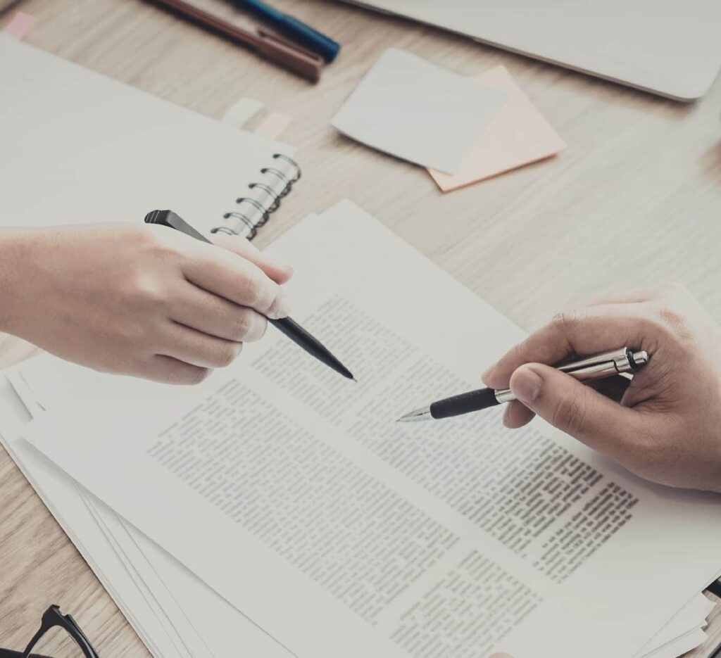 Two people reviewing and discussing documents while pointing at the text with pens.
