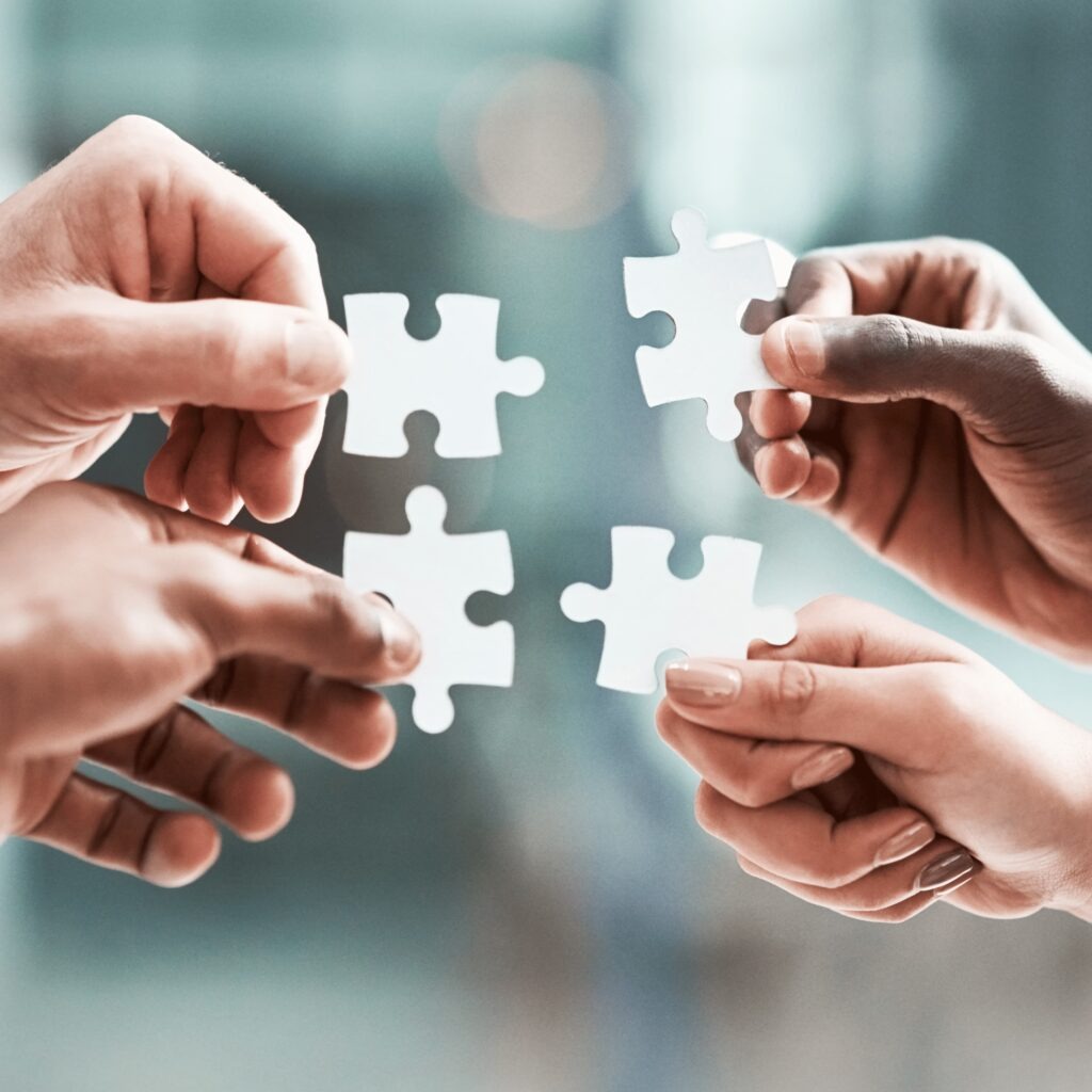 Hands holding puzzle pieces together, representing teamwork, problem solving, and collaboration.